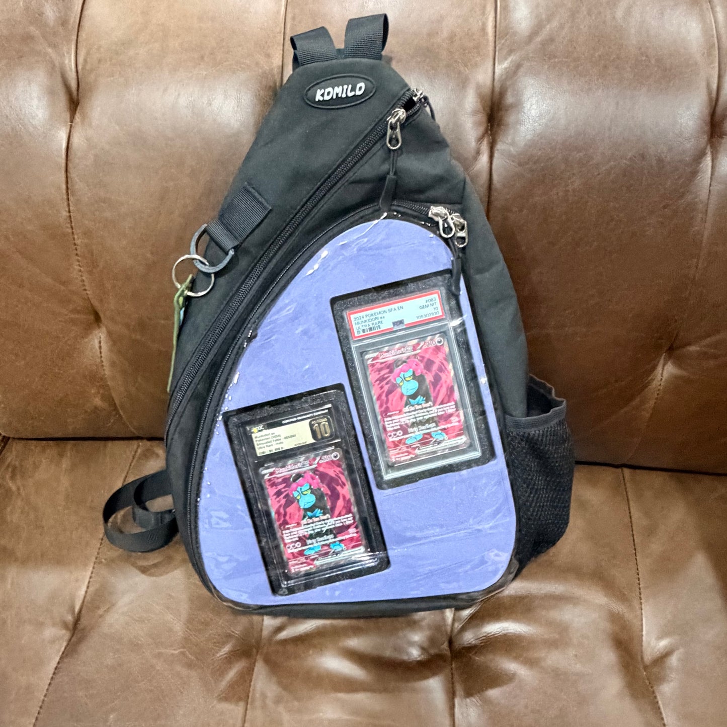 Black crossbody bag front with light blue insert showing graded Munkidori PSA and CGC slabs