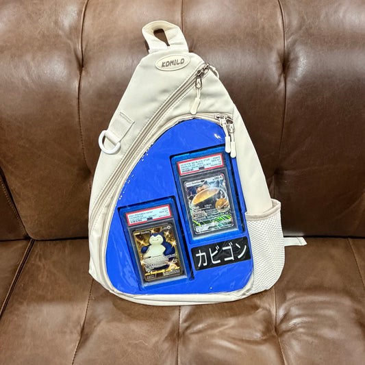 Cream KOMILO crossbody bag front with navy blue insert showing PSA graded Snorlax slabs and Kabigon nameplate