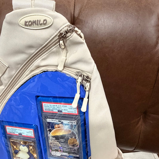 Close-up of cream KOMILO bag front panel showing PSA graded Snorlax GX cards and Kabigon nameplate insert